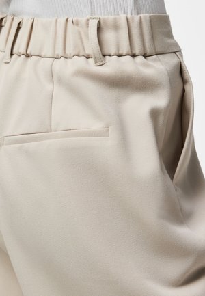 Kruusvalge elastse vöökohaga beežid püksid vöökonksude ja tagumise lipsuga taskuga, kantud sisse volditud valge soonikkta topsiga.