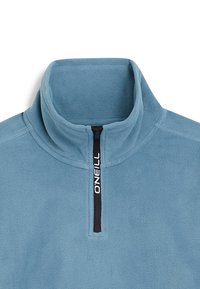 Lysblå fleecepullover med høj krave, halv lynlås og sort lynlås. Har "ONEILL" logoet i hvidt på lynlåsflappen.