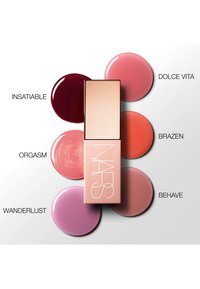 NARS lipproduct met een rechthoekige, matte perzikkleurige behuizing. De omringende tinten omvatten diep rood, zachte roze en gedempte mauve, die verschillende afwerkingen reflecteren.