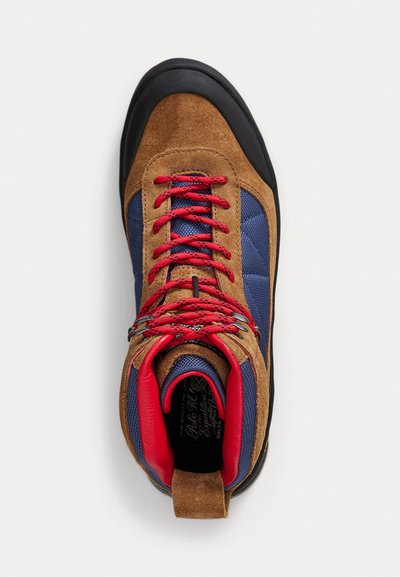 Scarpa da arrampicata in suede marrone e tessuto blu con lacci rossi, suola in gomma nera e colletto imbottito per supporto. Presenta occhielli metallici.