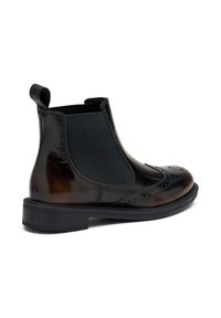 Botas Chelsea de cuero negro con paneles laterales elásticos, detalles de brogue y un acabado texturizado. Presentan una suela baja y robusta para mayor estabilidad.