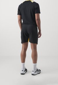 Czarne spodenki sportowe z żółtymi akcentami po bokach, w zestawieniu z czarną koszulką z krótkim rękawem z żółtym detalem przy kołnierzyku.