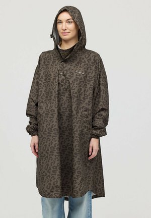 Vrouw draagt een lange, bruine regenponcho met luipaardprint, capuchon, elastische manchetten en drukknopen, staand tegen een effen lichte achtergrond.