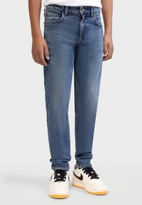 Ξεβαμμένο μπλε τζιν με ίσια γραμμή, πέντε τσέπες και αντίθετες ραφές. Συνδυασμένο με λευκά αθλητικά παπούτσια που έχουν μαύρες λεπτομέρειες.