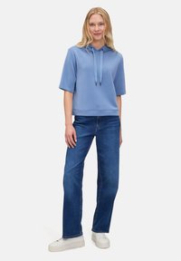 Jasnoniebieska bluza z kapturem z krótkim rękawem, z detalem w postaci sznurków i ściągaczem u dołu, w połączeniu z prostymi granatowymi dżinsami i białymi trampkami.