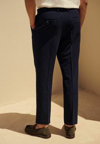 Pantalon texturé bleu marine avec une coupe droite, poches arrière et détails en bouton, associé à des mocassins en daim marron.
