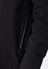 Giacca nera caratterizzata da un tessuto morbido e textured. I dettagli notevoli includono una tasca laterale con zip e un design pulito e minimal.