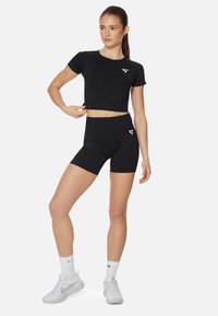 Set di abbigliamento sportivo nero composto da un crop top a maniche corte e pantaloni corti a vita alta, realizzato in materiale elasticizzato con un design elegante e dettagli con logo.