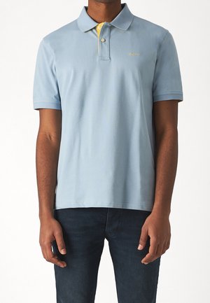 Koszulka polo z jasnoniebieskiej bawełny z żółtym akcentem na kołnierzyku. Posiada dwudzielny plisa zapinana na dwa guziki oraz subtelne haftowane logo na piersi.