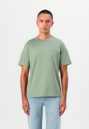 Light green cotton t-shirt with a round neck and short sleeves, featuring a small embroidered logo on the chest, paired with light blue jeans.