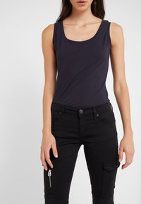 Marinblå ärmlös t-shirt med rund halsringning, kombinerad med åtsittande svarta cargobyxor med en sidoficka med dragkedja. Mjuk bomullsblandning.