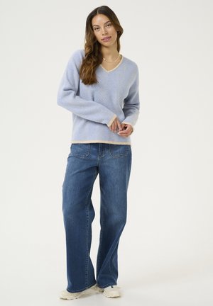 Lichtblauwe, textuurtrui met een V-hals en crèmekleurige afwerking, gecombineerd met losse blauwe jeans en witte sneakers. Eenvoudige en casual outfit.