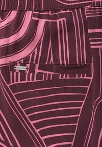 Poche arrière sur tissu bordeaux avec des lignes géométriques roses abstraites et une petite étiquette métallique portant la mention "Street One."