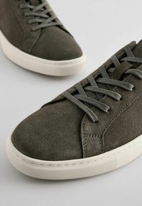 Sive sneakers od nubuk kože s okruglim vrhom, ravnim bijelim gumenim potplatom i odgovarajućim sivim vezicama. Istaknuti detalji šivanja duž bočnih strana.