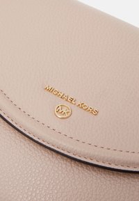 Růžová texturovaná kožená kabelka s zlatým logem "MICHAEL KORS" a kulatým emblémem MK na přední straně. Disponuje hladkým, zakřiveným uzavíráním na klopě.