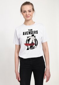 Biała koszulka bawełniana z graficznym nadrukiem, który zawiera tekst "ZESPÓŁ AVENGERS" oraz ikoniczny logo zaprojektowane w czarne i czerwone akcenty.