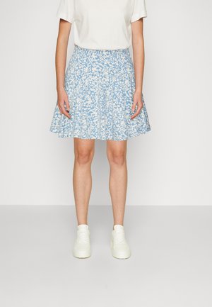Jupe évasée bleu clair avec un motif floral blanc, taille élastique et longueur au genou. Portée avec un t-shirt blanc et des baskets blanches.
