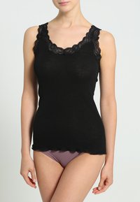 Top in cotone nero a costine con pizzo scallopato lungo il collo, forma aderente e orlo leggermente curvato. Indossato con pantaloni di un leggero colore viola.