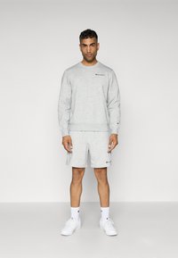 Gray fleece sweatshirt and shorts set with logo accents; features crew neck, ribbed cuffs, and matching color, complemented by white sneakers.