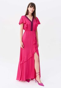 Rosa Maxikleid mit Rüschensäumen und tiefem V-Ausschnitt. Verfügt über einen Seitenschlitz und strukturierte Akzente entlang des Ausschnitts.