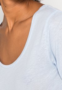 Vaaleansininen lyhytnuttuinen paita, joka on valmistettu pehmeästä kankaasta ja jossa on pyöreä kaula-aukko. Paidassa on hieno rakenne ja rento leikkaus.