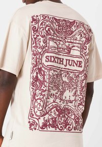 Beżowa bawełniana koszulka z dużą burgundową grafiką na plecach, skomplikowanymi wzorami oraz napisem "SIXTH JUNE" i okrągłym dekoltem.