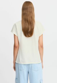 Lys beige t-shirt med korte ærmer, afslappet pasform, glat tekstur og rundet kant. Et par lyseblå cargobukser med lomme detaljer.