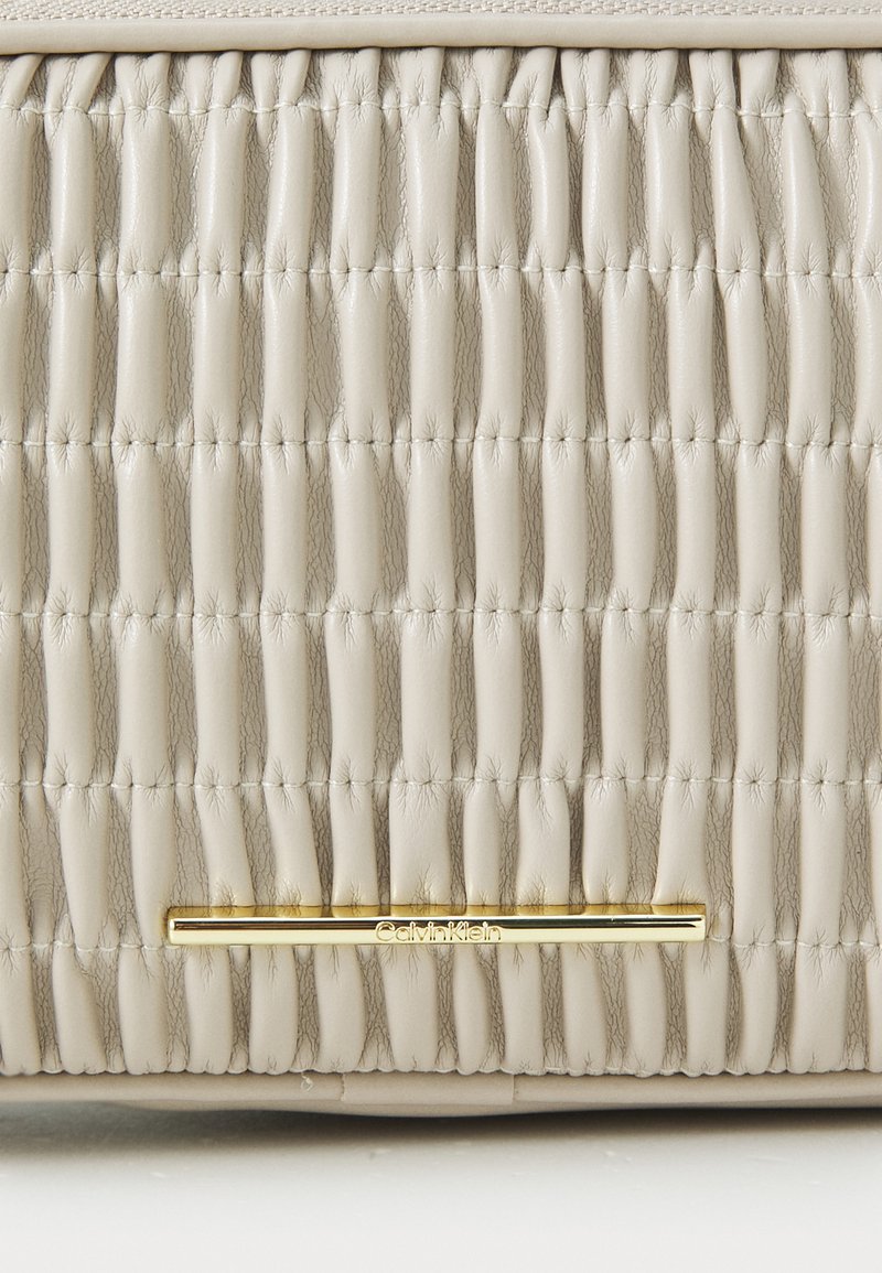 Beżowa skórzana torba o pikowanej fakturze, z złotym akcentem logo Calvin Klein i usprawnionym, prostokątnym kształtem.