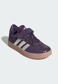 Fialové semišové tenisky s kovovými akcenty a bílými pruhy. Mají polstrovaný límec a robustní růžovou gumovou podrážku. Uzávěr se dá nastavit.