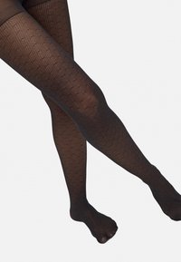 Pantys negras con un diseño de malla texturizada, que presentan pequeños patrones de puntos en toda su superficie. La tela parece translúcida y elástica.