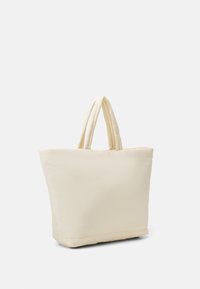 Sac fourre-tout beige en tissu doux, avec deux anses solides, une forme rectangulaire et une texture lisse sans motifs visibles.