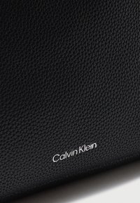 Μαύρη επιφάνεια από υφή δέρματος με μικρό λευκό λογότυπο Calvin Klein χαραγμένο κοντά στην κάτω άκρη.