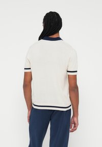 Polo majica s kratkimi rokavi v kremni barvi z mornarsko modrim ovratnikom in robnimi poudarki. Tkanina ima mehak otip in sproščen kroj. Enostaven dizajn s kontrastnimi črtami.