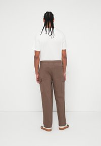 Pantaloni cargo marroni con tasche laterali, abbinati a una t-shirt bianca a maniche corte, visti da dietro. Tessuto morbido e vestibilità rilassata.