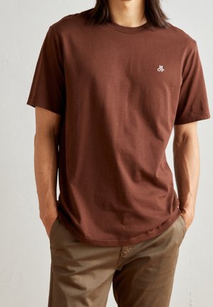 Brązowy bawełniany t-shirt z okrągłym dekoltem, krótkimi rękawami i małym białym logo na lewej piersi. Miękka tekstura i luźny fason.