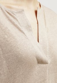 Top in maglia beige con scollo a V, morbida al tatto e con un delicato motivo mélange, dalla vestibilità comoda e maniche corte.