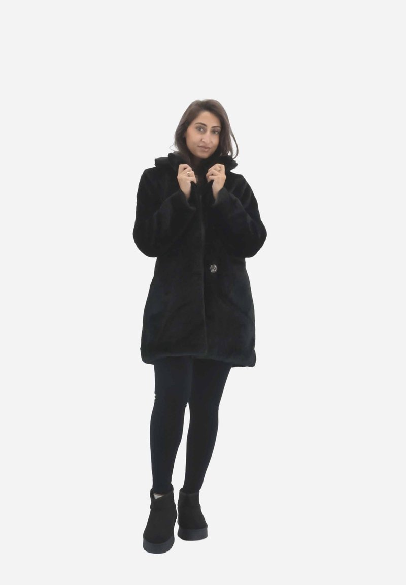 Sort pelsjakke med hætte, udstyret med en enkelt knaplukning. Glat tekstur, knælængde design kombineret med sorte leggings og ankelstøvler.