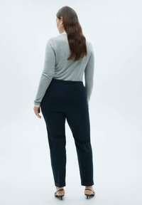 Haut gris à manches longues associé à un pantalon tailoring bleu foncé. Le pantalon présente une texture lisse et de discrètes poches arrière. Sandales noires à talons.