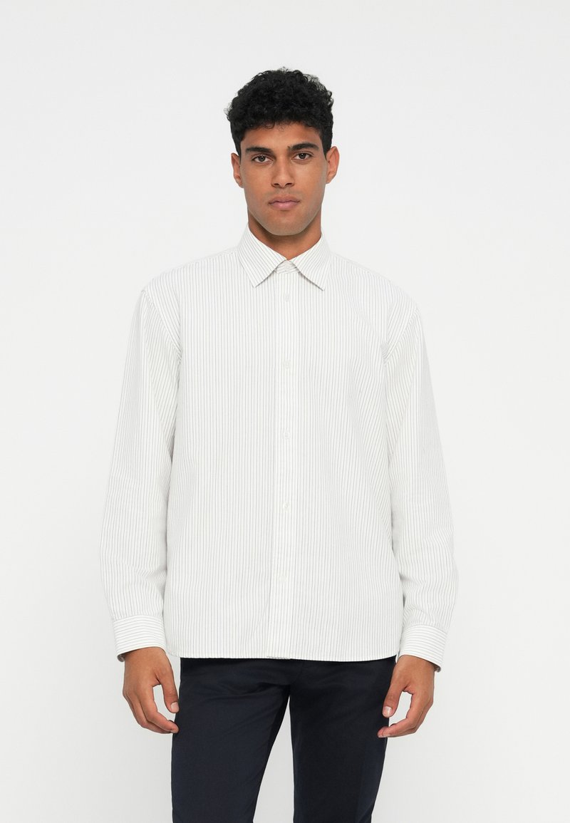 Camicia bianca a manica lunga con sottili righe verticali, chiusura con bottoni sul davanti e colletto classico. Il tessuto sembra leggero e liscio.