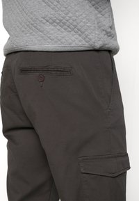Dark cargo pants made of lightweight fabric, featuring side pockets, a back pocket with a button, and a smooth texture.