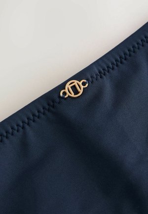 Chilot de bikini bleumarin din material neted, cu accesorii decorative din aur și detalii de cusătură distincte pe talie.