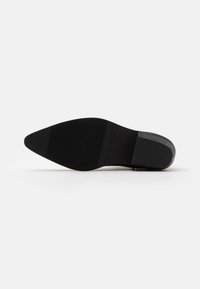 Sohle eines Schuhs mit spitzer Zehenform, aus Gummi gefertigt, mit einer strukturierten schwarzen Oberfläche, horizontalen Rillen und einem flachen Absatz.