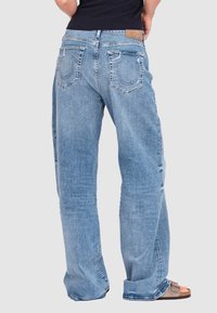 Jasnoniebieskie dżinsy o luźnym kroju, z dwoma tylnymi kieszeniami i subtelnymi detalami przeszyłkowymi. Noszone z jasnobrązowymi sandałami.