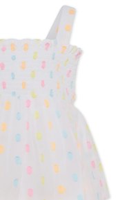 Robe sans manches blanche avec un corsage smocké, ornée de pois colorés en jaune, rose et bleu sur un superposé transparent.
