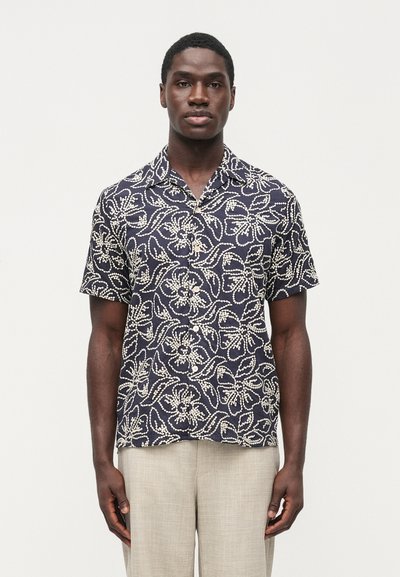 Chemise à manches courtes en tissu bleu marine avec motifs floraux et feuillus blancs. Devant boutonné avec une coupe décontractée et un col.