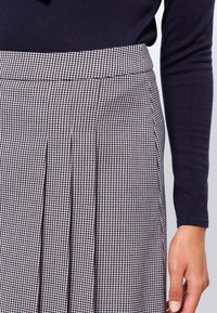 Gonna a quadri in tessuto bianco e nero, con pieghe, un punto vita sartoriale e una texture liscia. Indossata con una maglia scura a maniche lunghe.