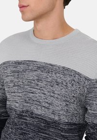 Pulover tricotat în nuanțe de gri și bleumarin, cu un model texturat, guler circular și dungi orizontale contrastante. Material moale, de greutate medie.