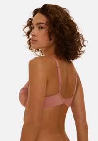 Soutien-gorge rose pâle avec détails floraux brodés, armatures, bretelles réglables et fermeture à agrafes dans le dos. Texture de tissu lisse.