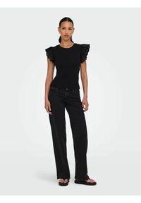 Sort ribbet top med dekorative sorte blondeslag med rynker, parret med løstsiddende sorte jeans og flade sorte sandaler.