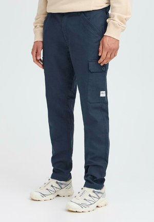 Navy cargo pants with side pockets, button accents, and a branded label; made of durable fabric with a smooth texture.